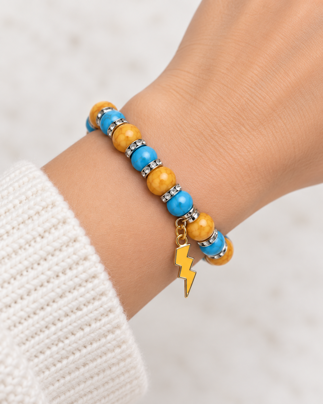 Blue and golden yellow beaded bracelet with silver-tone spacers and lightning charm worn on wrist